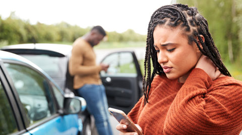 Stressed woman types on phone after car accident